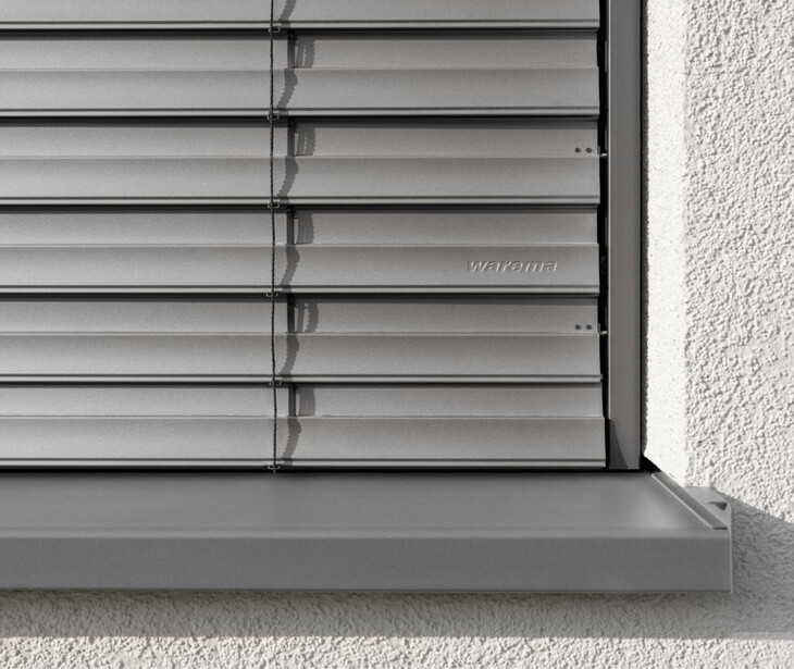 Primo piano di una tapparella grigia chiusa con la scritta warema su una parete bianca.