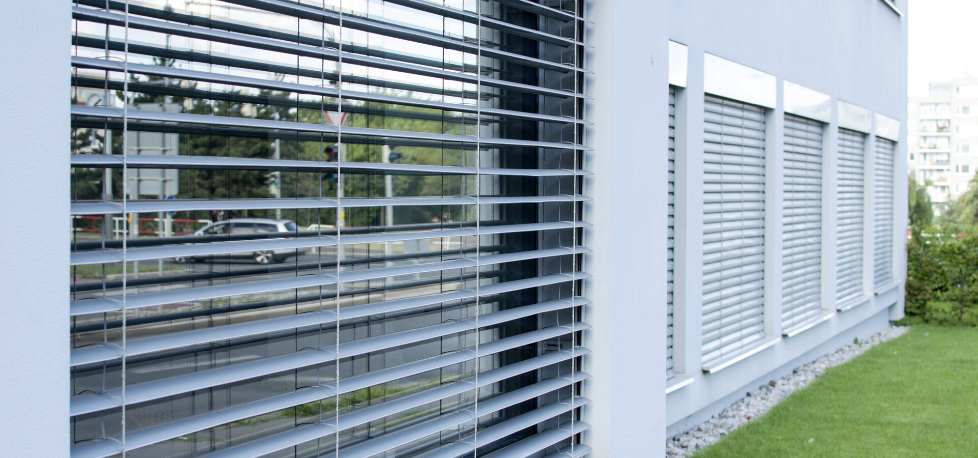 Fassade eines modernen Gebäudes mit geschlossenen Jalousien und grünem Rasen davor.