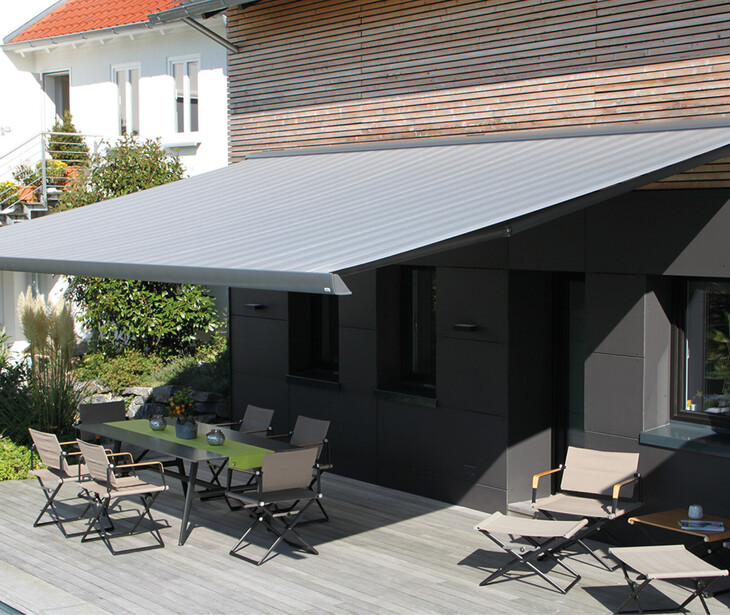 Terrasse mit ausfahrbarer Markise, Tisch und Stühlen vor einem modernen Haus.