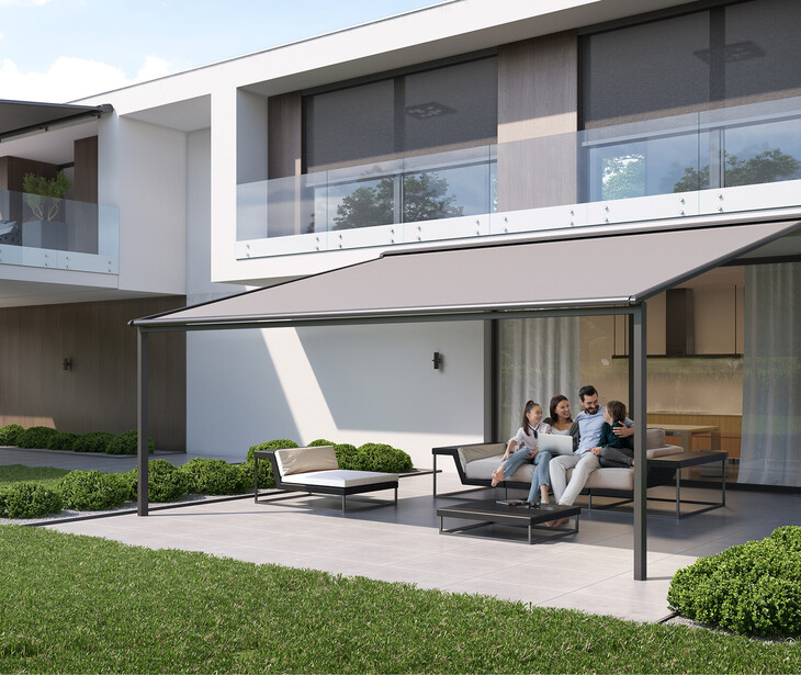 Moderner zweistöckiger Wohnhaus mit großer Glasfront und überdachter Terrasse, auf der eine Familie auf einer Sitzgruppe entspannt.
