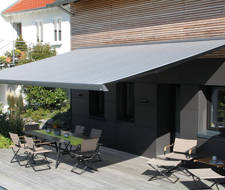 Terrazza con tenda da sole estensibile, tavolo e sedie davanti a una casa moderna.