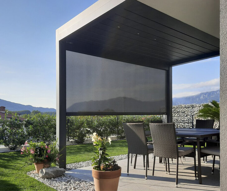 Moderner überdachter Sitzbereich mit Tisch und Stühlen auf Terrasse neben bepflanztem Garten und Berglandschaft im Hintergrund.