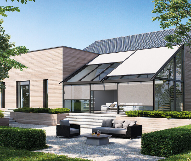 Casa moderna con tetto piano, terrazza vetrata e tende da sole per la veranda, immersa in un giardino con cespugli e alberi.