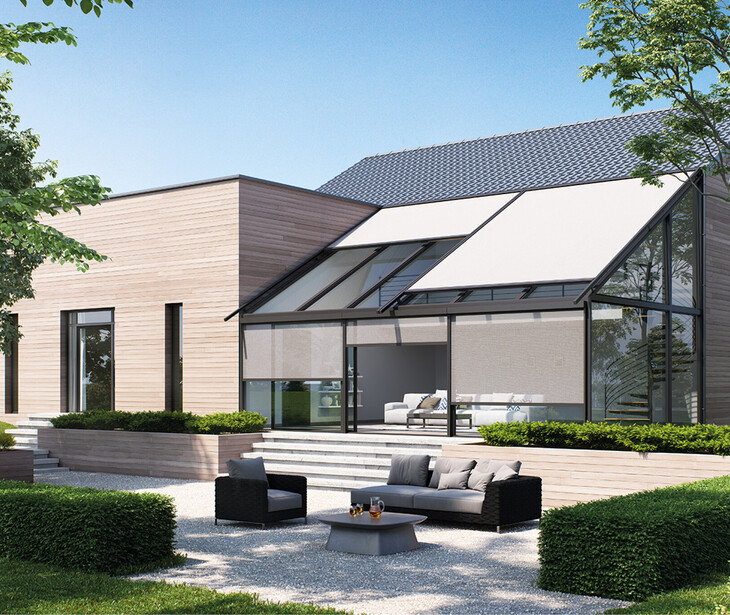 Modernes Haus mit Flachdach, verglaster Terrasse und Wintergartenmarkiesen in einem Garten mit Büschen und Bäumen.